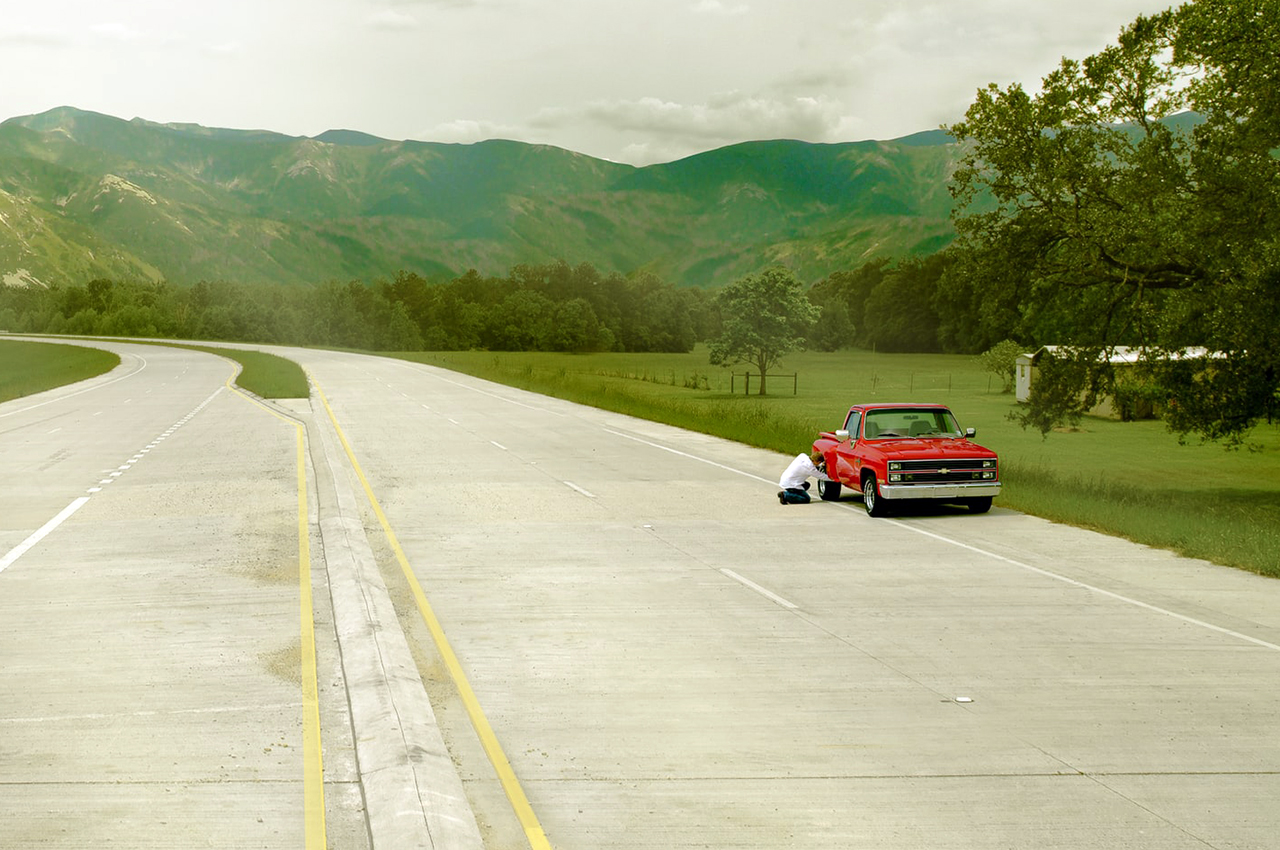 A red pickup truck broken down on the side of a highway