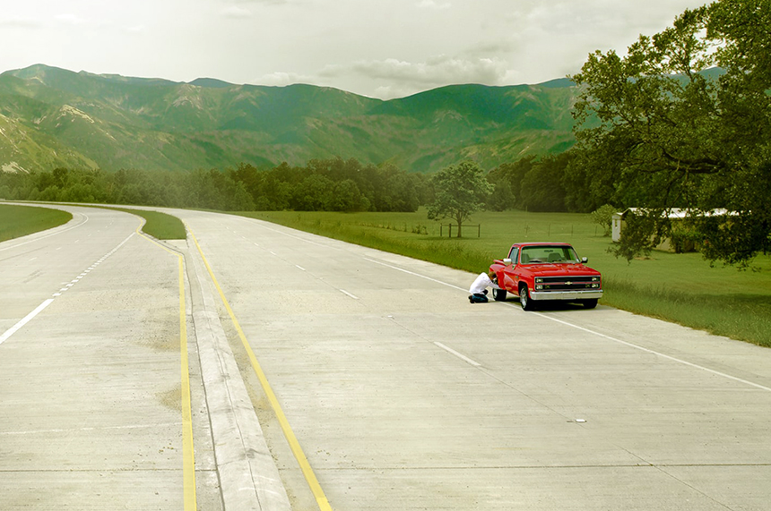 A red pickup truck broken down on the side of a highway