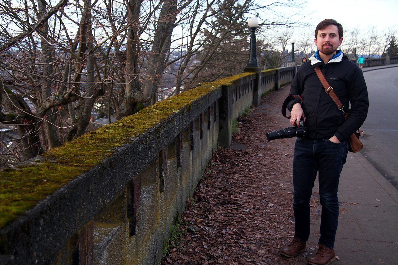 A man holding a camera along a mossy ledge